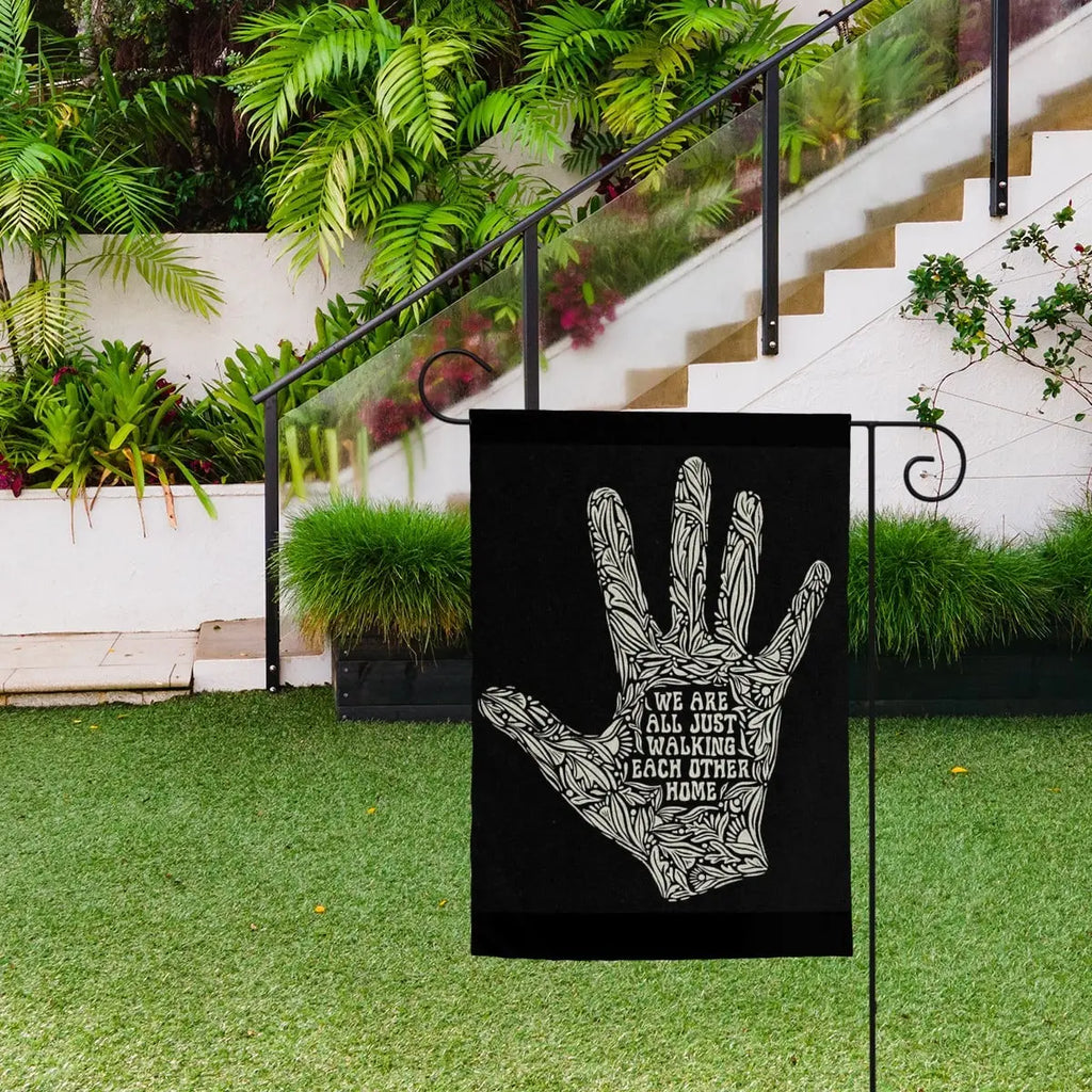 Sandy Beach garden decor flag with the message "We Are All Just Walking Each Other Home" displayed outdoors.